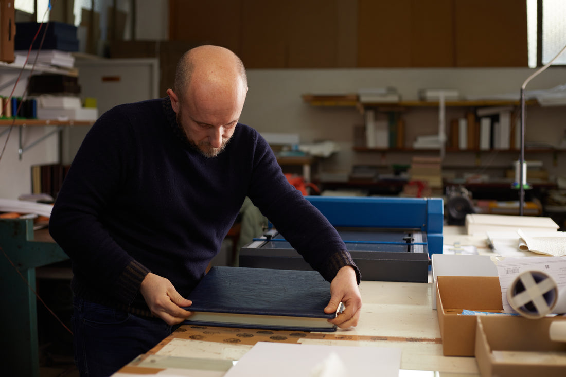 Man in a black sweater meticulously leather binding a book for Kadri Books